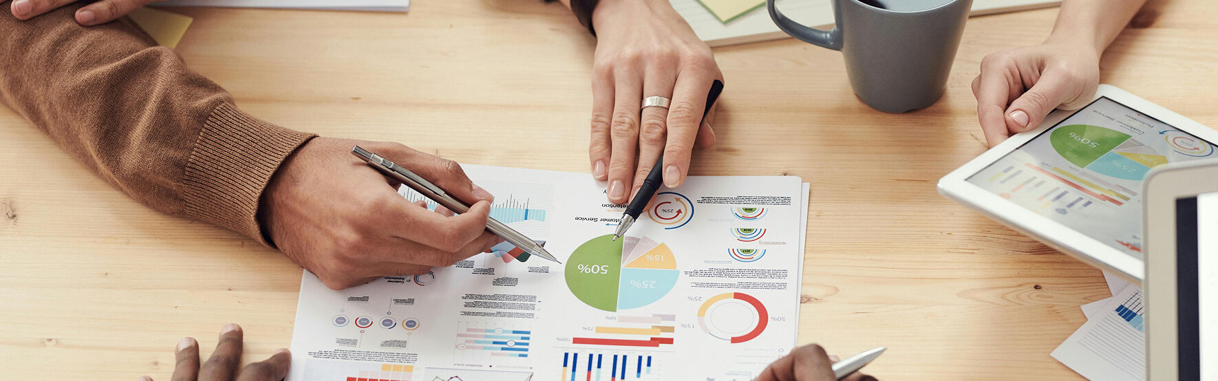 Daten Analyse Marketing Hände von drei Personen auf einem Papier voll mit bunten Statistiken