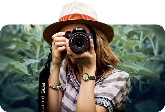 Fotografin vor Pflanzenhintergrund Frau hält Kamera vor Gesicht, Hintergrund Pflanzen